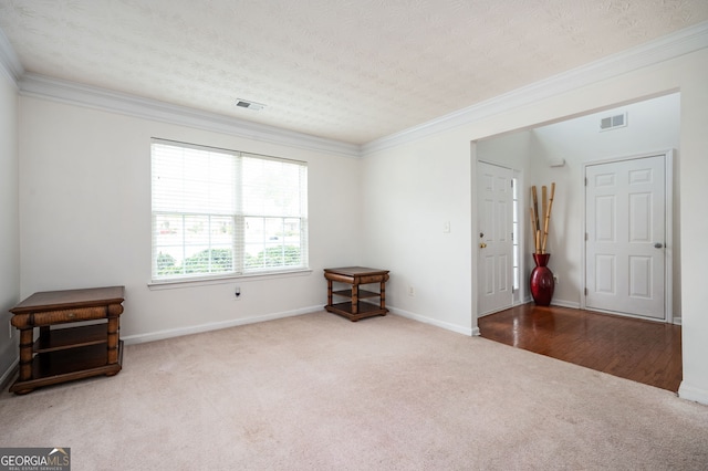 carpeted spare room with visible vents, a textured ceiling, baseboards, and ornamental molding