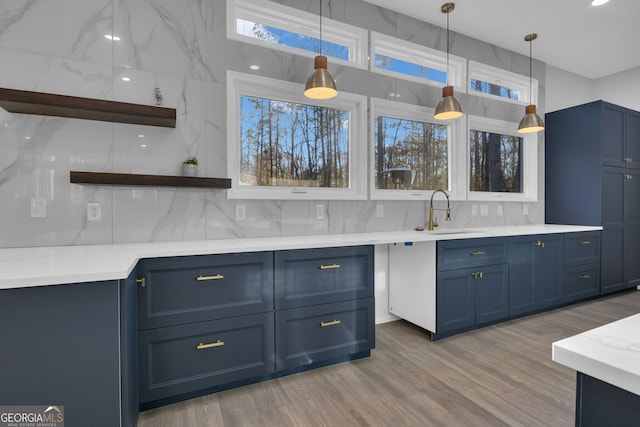 kitchen featuring pendant lighting, blue cabinets, sink, tasteful backsplash, and wood-type flooring