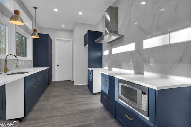 kitchen with wall chimney exhaust hood, stainless steel microwave, sink, blue cabinetry, and hanging light fixtures