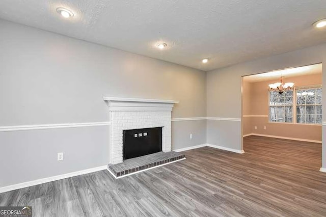 unfurnished living room featuring a notable chandelier, dark hardwood / wood-style flooring, a textured ceiling, and a brick fireplace