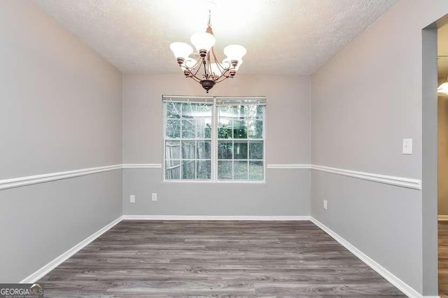 unfurnished dining area with dark hardwood / wood-style flooring, a textured ceiling, and an inviting chandelier