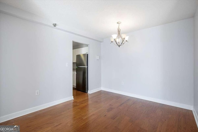 spare room with hardwood / wood-style flooring and an inviting chandelier