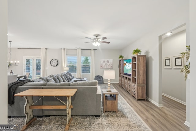 living room with ceiling fan with notable chandelier and light hardwood / wood-style floors