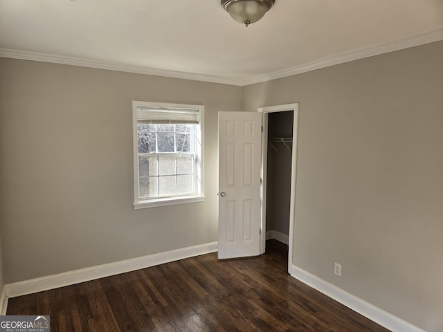 unfurnished bedroom featuring crown molding, a spacious closet, dark wood-type flooring, and a closet