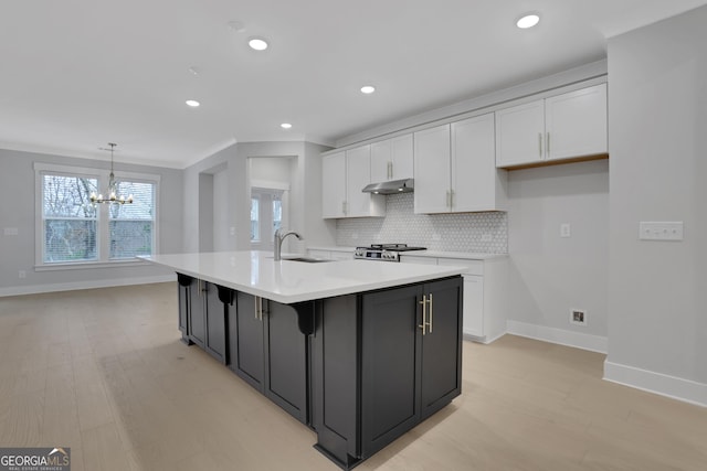 kitchen featuring a center island with sink, decorative light fixtures, white cabinetry, and light hardwood / wood-style flooring