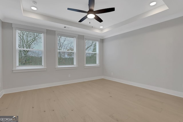 unfurnished room featuring light wood-type flooring, a tray ceiling, and ceiling fan