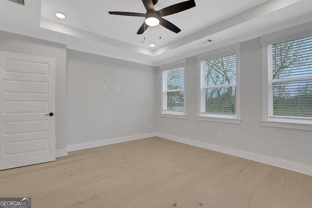 spare room featuring light wood-type flooring, a raised ceiling, and ceiling fan