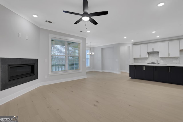 unfurnished living room with ceiling fan with notable chandelier, light hardwood / wood-style floors, and sink