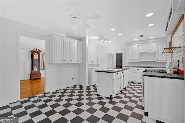 kitchen with ceiling fan, sink, washing machine and clothes dryer, white cabinets, and a center island