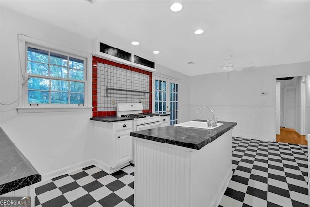 kitchen with backsplash, sink, ceiling fan, white gas stove, and white cabinetry