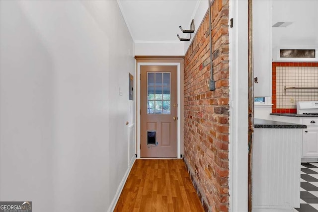 doorway with light hardwood / wood-style floors, crown molding, and brick wall