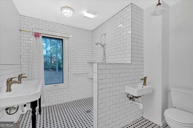 bathroom with tiled shower, tile patterned floors, toilet, and tile walls