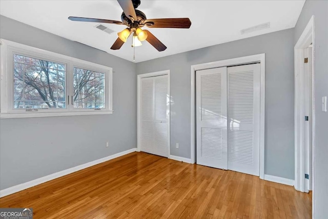 unfurnished bedroom featuring light wood-type flooring, two closets, and ceiling fan