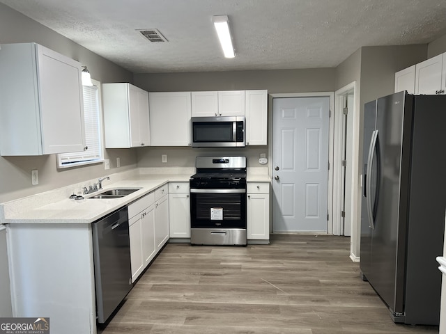 kitchen with white cabinets, sink, light wood-type flooring, a textured ceiling, and stainless steel appliances