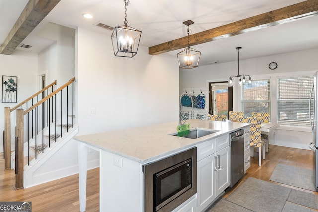 kitchen featuring built in microwave, a kitchen island with sink, sink, pendant lighting, and beamed ceiling