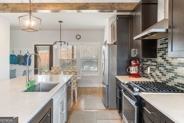 kitchen with pendant lighting, wall chimney exhaust hood, light stone countertops, a notable chandelier, and stainless steel appliances