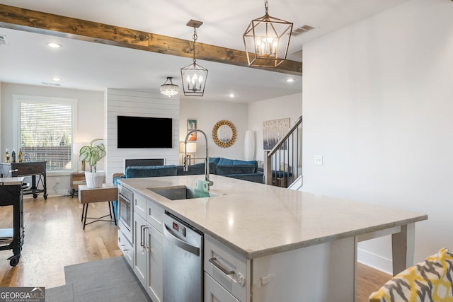 kitchen with appliances with stainless steel finishes, a large fireplace, sink, a center island with sink, and decorative light fixtures