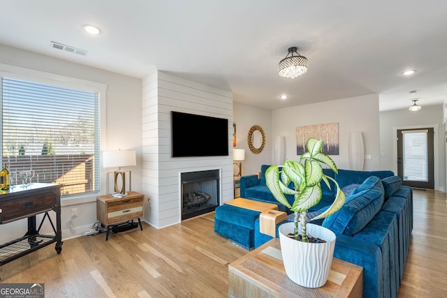 living room featuring a large fireplace, light wood-type flooring, and a wealth of natural light