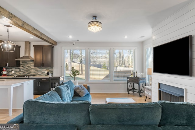 living room featuring beam ceiling, light wood-type flooring, and an inviting chandelier