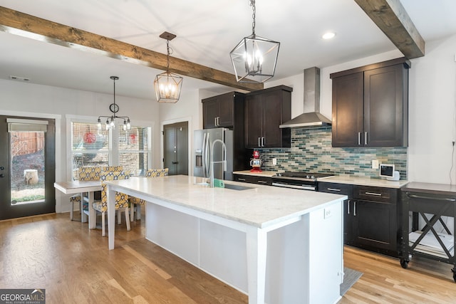 kitchen featuring stainless steel appliances, a kitchen island with sink, wall chimney exhaust hood, and pendant lighting