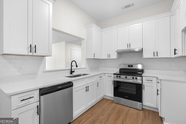 kitchen with tasteful backsplash, stainless steel appliances, sink, white cabinets, and hardwood / wood-style floors