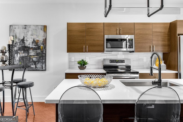 kitchen with hardwood / wood-style floors, sink, appliances with stainless steel finishes, tasteful backsplash, and a kitchen bar