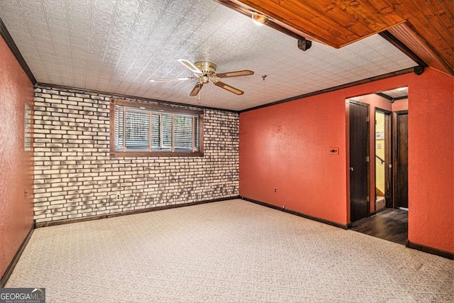 carpeted empty room featuring ceiling fan, ornamental molding, and brick wall