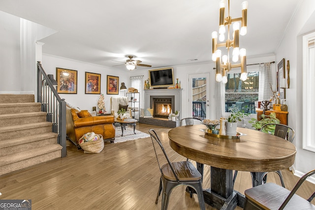 dining room featuring dark hardwood / wood-style flooring, ceiling fan with notable chandelier, a brick fireplace, and ornamental molding