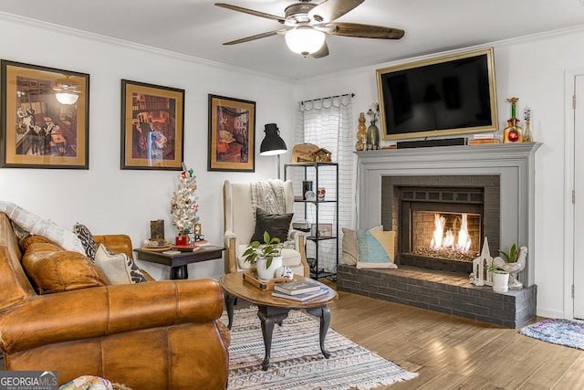 living room featuring ceiling fan, wood-type flooring, ornamental molding, and a brick fireplace