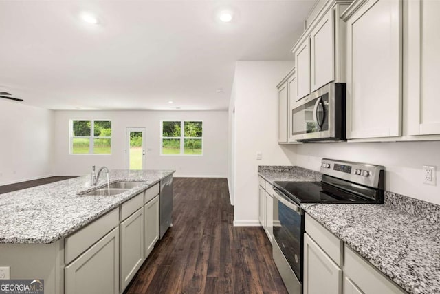 kitchen with sink, light stone counters, dark hardwood / wood-style flooring, an island with sink, and appliances with stainless steel finishes