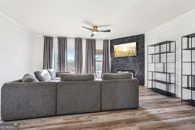 living room featuring a premium fireplace, ceiling fan, wood-type flooring, and ornamental molding