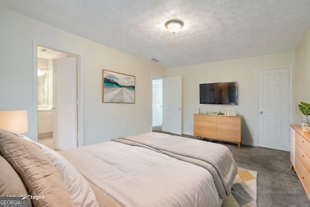 bedroom featuring ensuite bath, a textured ceiling, and dark colored carpet