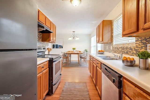 kitchen with appliances with stainless steel finishes, pendant lighting, sink, decorative backsplash, and light hardwood / wood-style floors