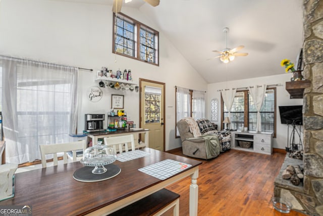 dining space with ceiling fan, dark hardwood / wood-style floors, a stone fireplace, and high vaulted ceiling