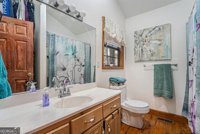 bathroom featuring wood-type flooring, toilet, vanity, and vaulted ceiling