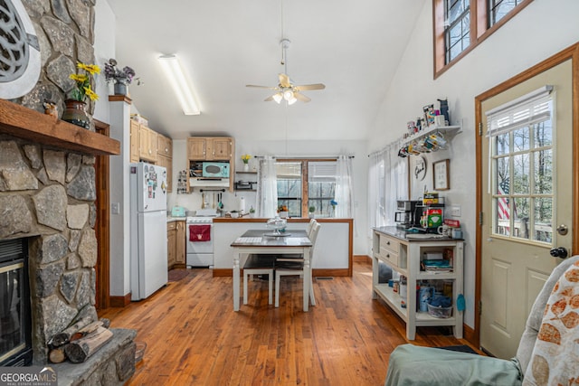 dining area featuring ceiling fan, high vaulted ceiling, a stone fireplace, and light wood-type flooring