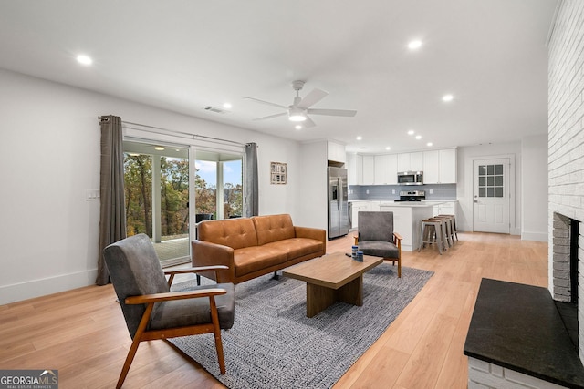 living room featuring ceiling fan, light hardwood / wood-style floors, and a fireplace