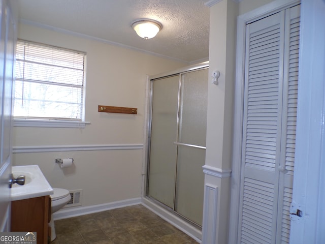 bathroom featuring toilet, a textured ceiling, ornamental molding, vanity, and a shower with door