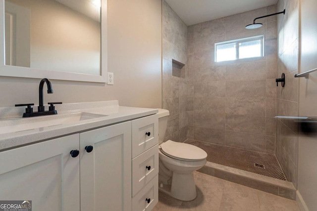 bathroom with a tile shower, tile patterned flooring, vanity, and toilet