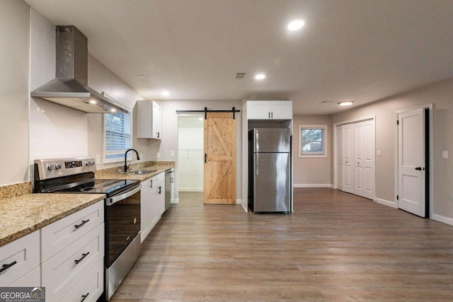 kitchen featuring a healthy amount of sunlight, wall chimney range hood, a barn door, white cabinets, and appliances with stainless steel finishes