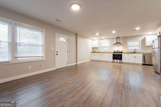 kitchen with white cabinetry, sink, wall chimney range hood, appliances with stainless steel finishes, and hardwood / wood-style flooring