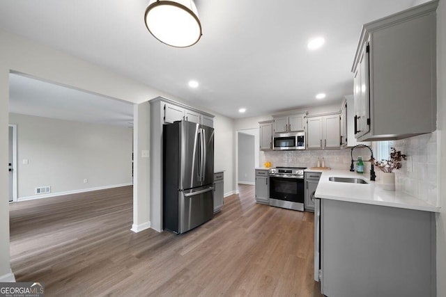 kitchen with stainless steel appliances, gray cabinets, hardwood / wood-style flooring, and sink