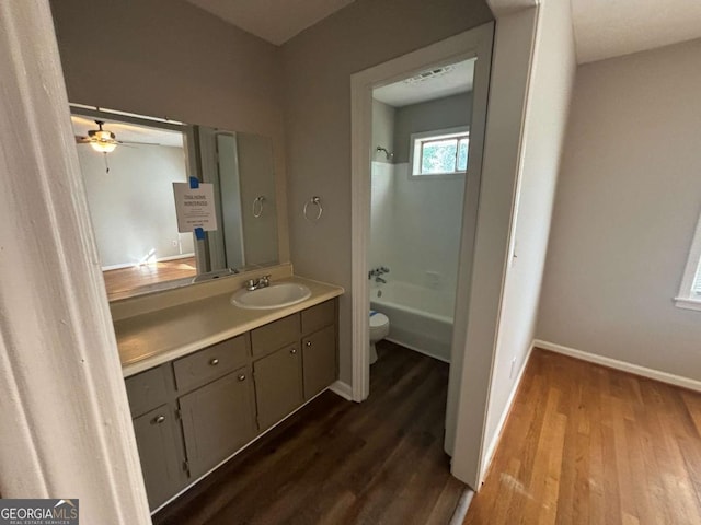 full bathroom featuring ceiling fan, hardwood / wood-style floors, toilet, vanity, and bathtub / shower combination