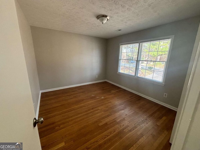 empty room with a textured ceiling and dark wood-type flooring