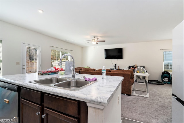 kitchen featuring light carpet, stainless steel dishwasher, dark brown cabinetry, a kitchen island with sink, and sink