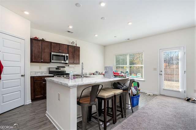 kitchen featuring a kitchen bar, dark hardwood / wood-style flooring, stainless steel appliances, sink, and an island with sink