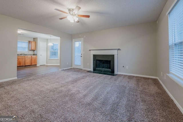 unfurnished living room featuring a textured ceiling, carpet floors, ceiling fan, and sink