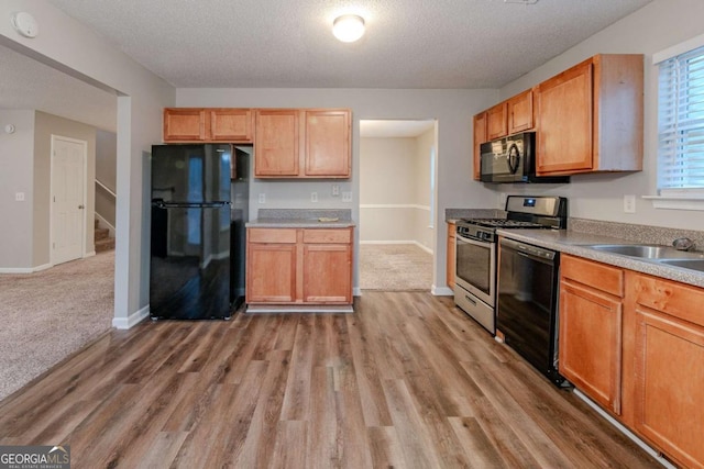 kitchen featuring sink, a textured ceiling, light wood-type flooring, and black appliances