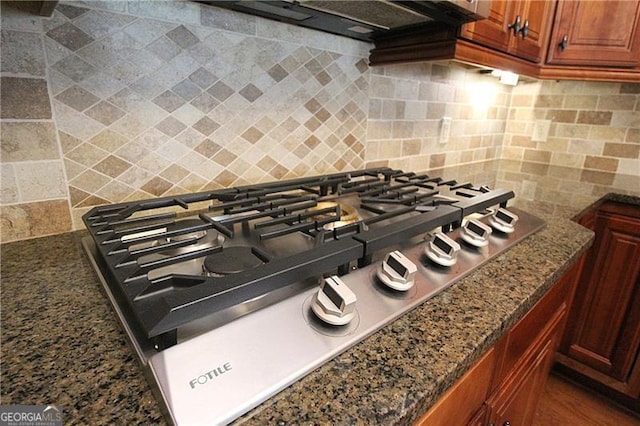 kitchen view of stainless steel gas stovetop, decorative backsplash, and brown cabinets