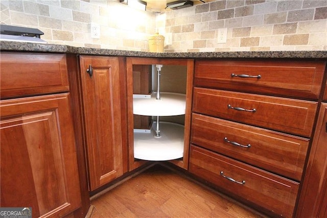 kitchen view of decorative backsplash, brown cabinets, stone countertops, and wood finished floors
